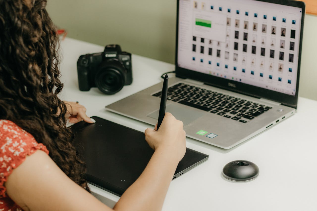 A woman using a graphics tablet and laptop, reviewing photos. Ideal for creative workspace themes.