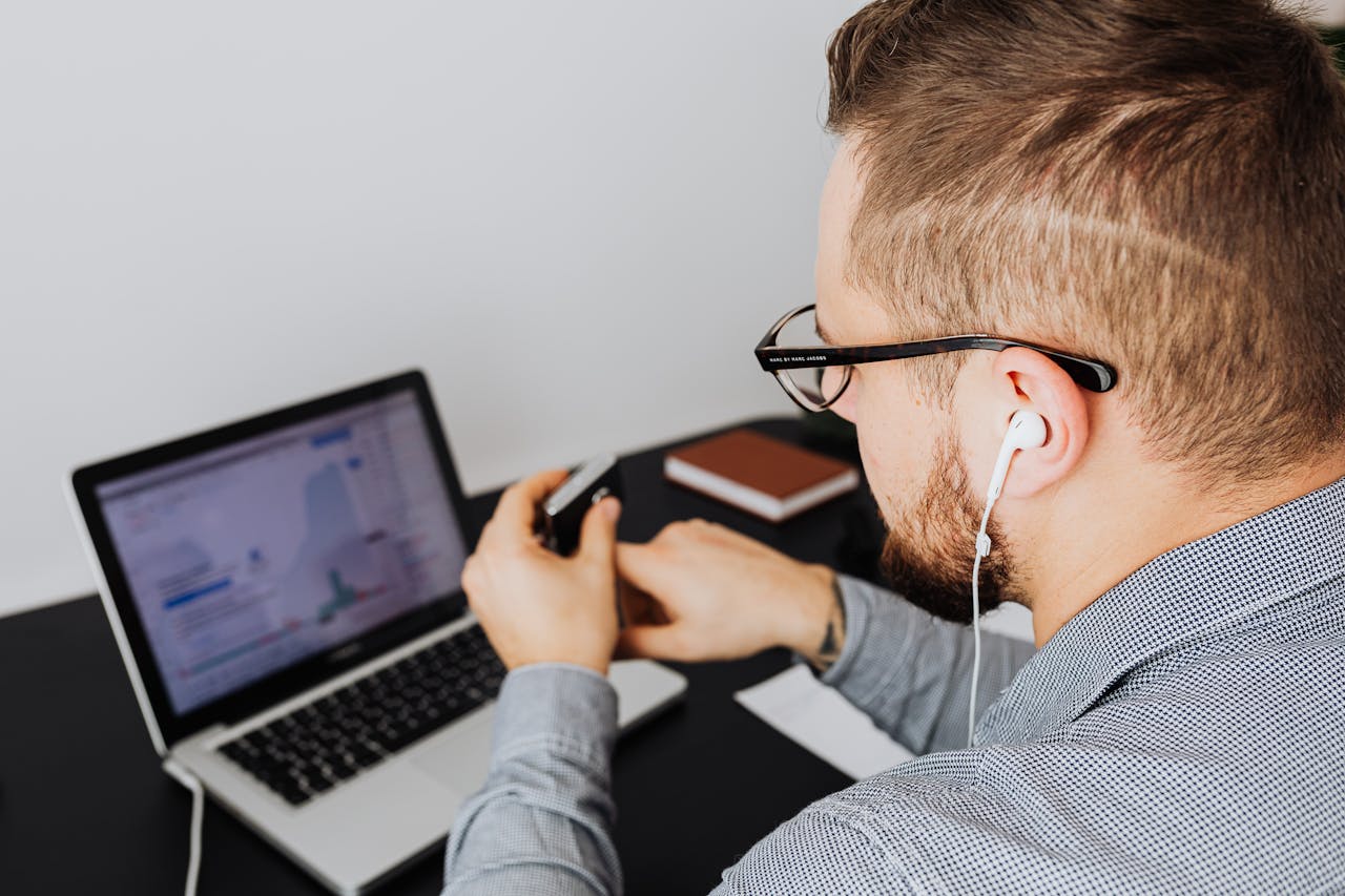 A business professional uses a laptop with charts and graphs while wearing earphones in an office setting.